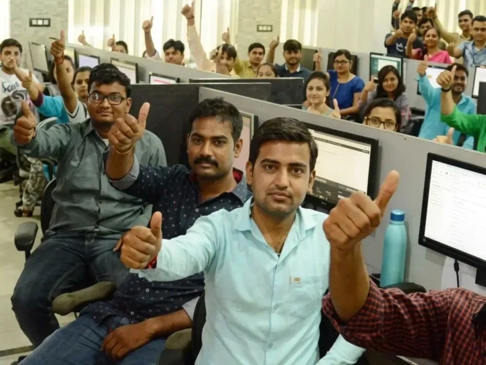 Keshav Infotech team members at their desks in the Rajkot studio, smiling and giving a thumbs up